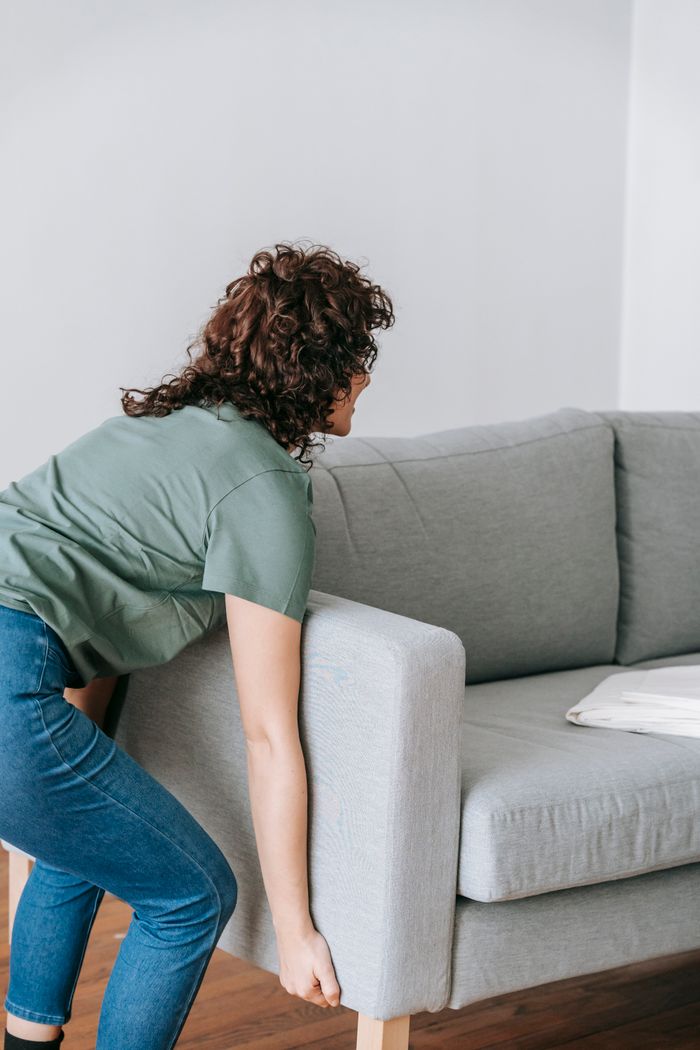 A woman lifting a sofa while rearranging furniture in a contemporary home setting.